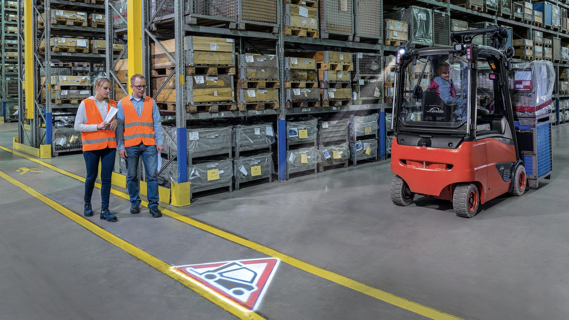 Two people walk in the warehouse and cross with a forklift truck